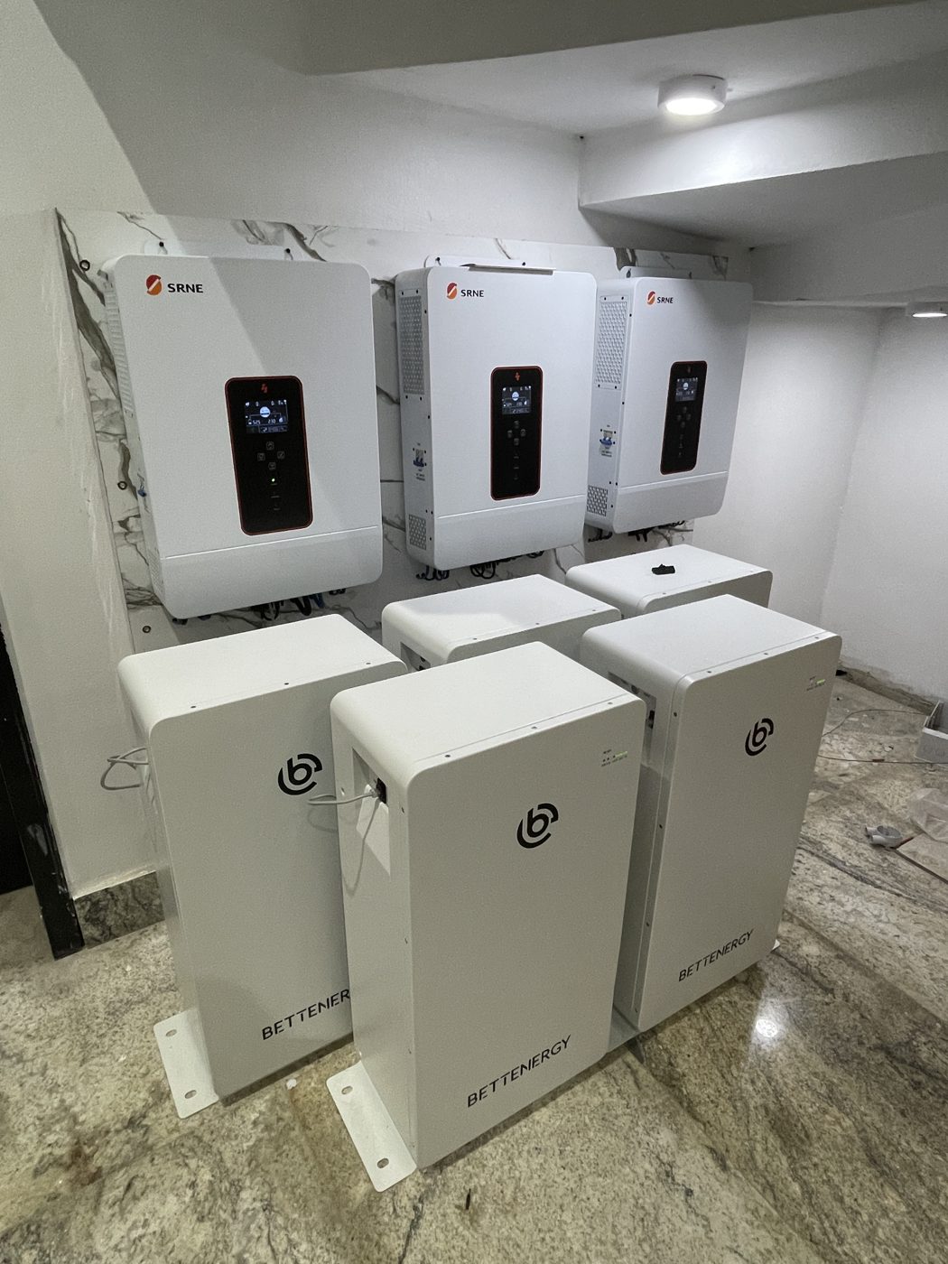 Three wall-mounted solar inverters above a bank of floor-standing batteries