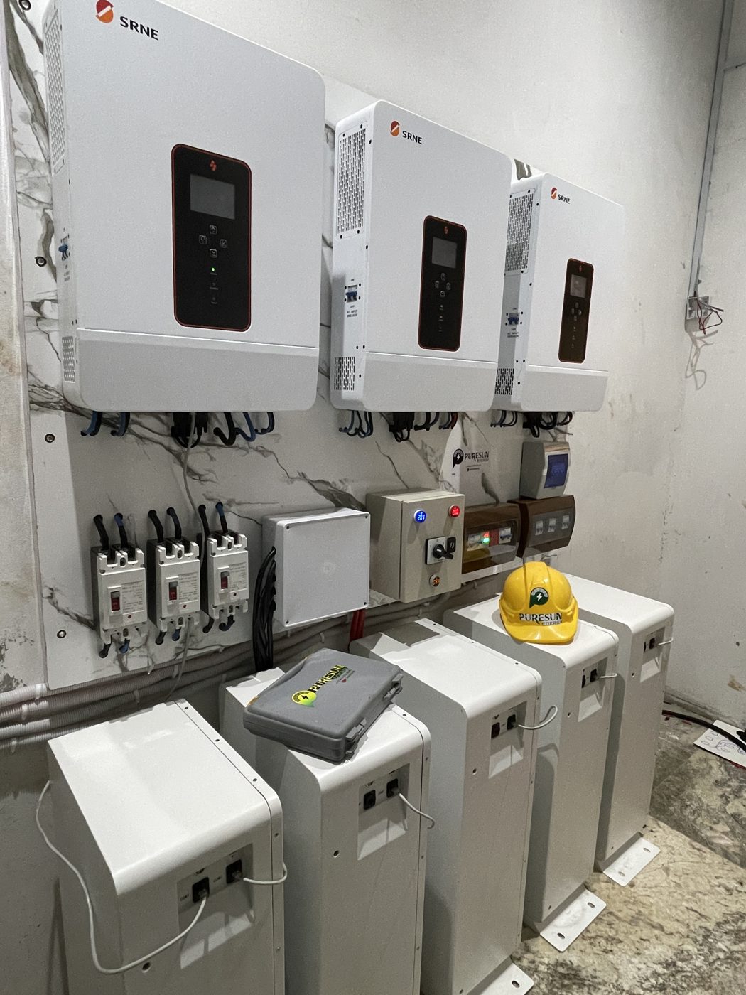 Solar inverters, circuit breakers and a changeover switch wired on one panel above five batteries